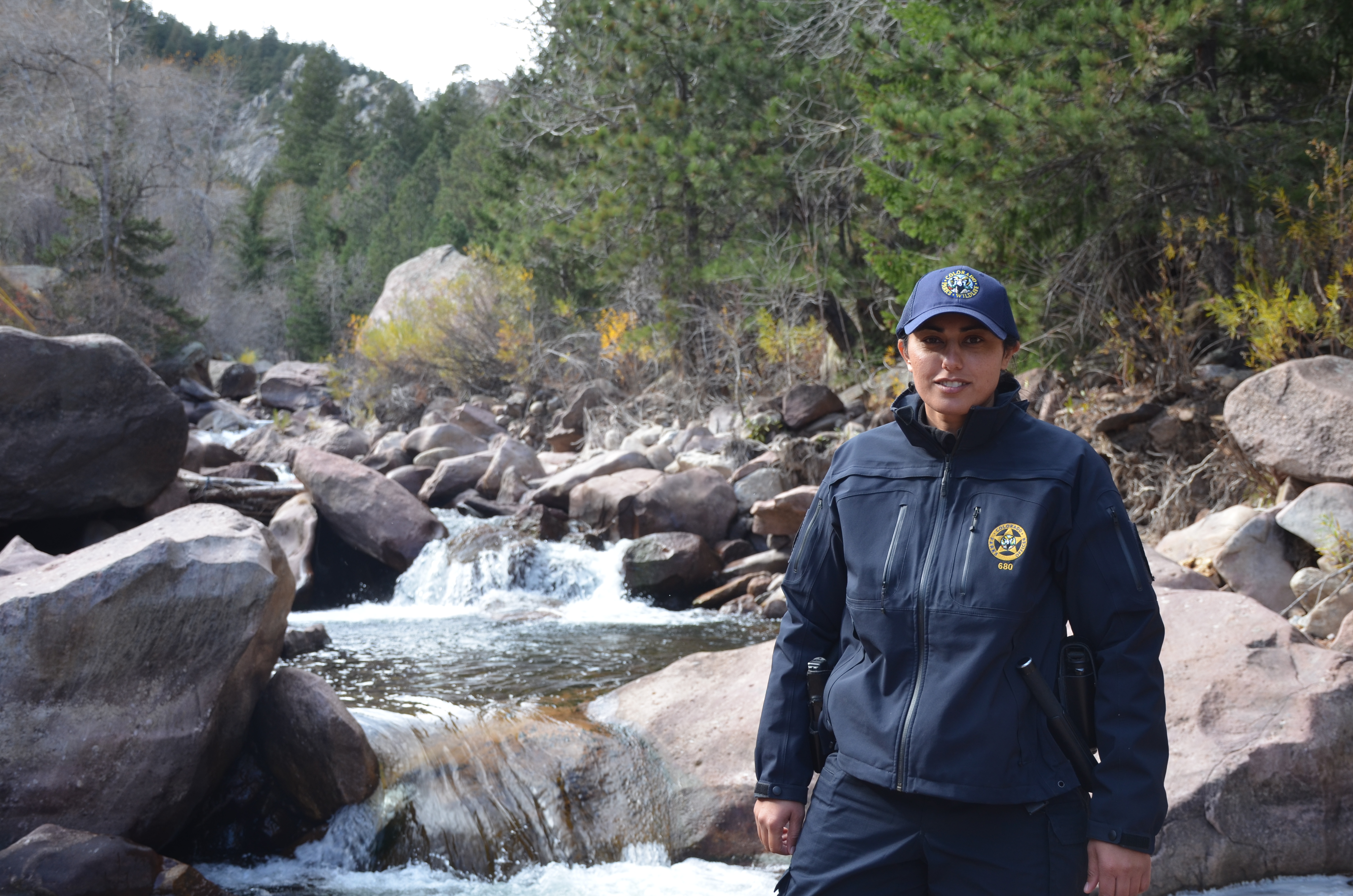 A female park ranger smiles as she stands in front of a river.