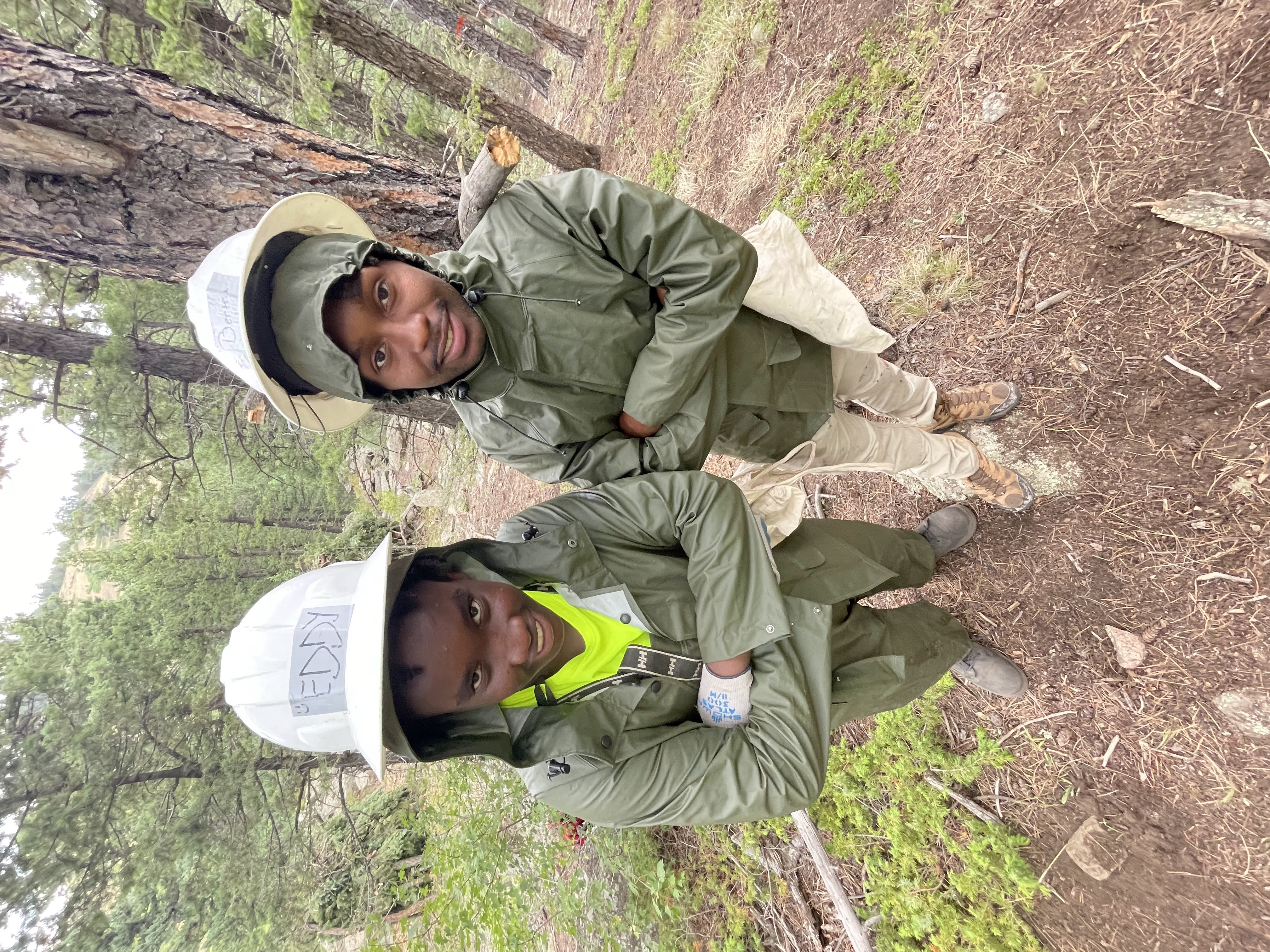 Two crew members doing a silly pose with arms crossed and smiling towards the camera in rain gear and PPE.