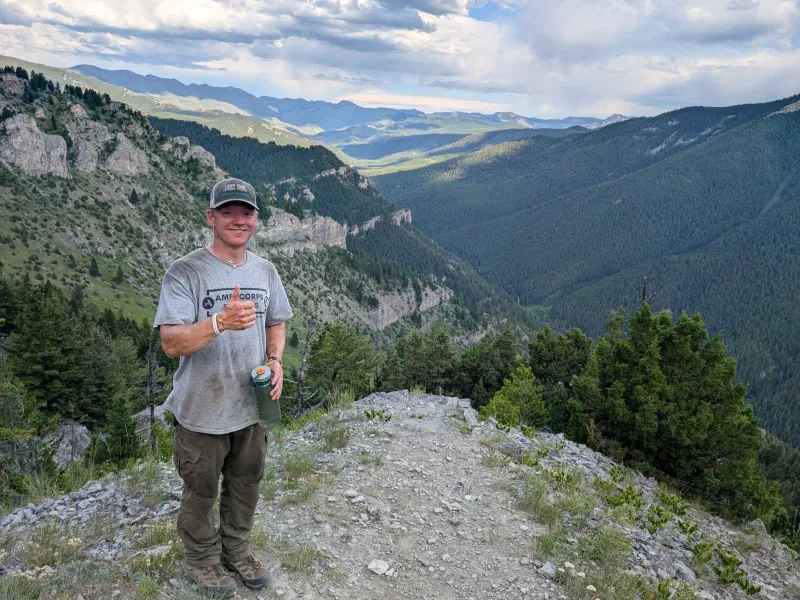 Andrew Birks stands on top of a mountain with more mountains in the distance