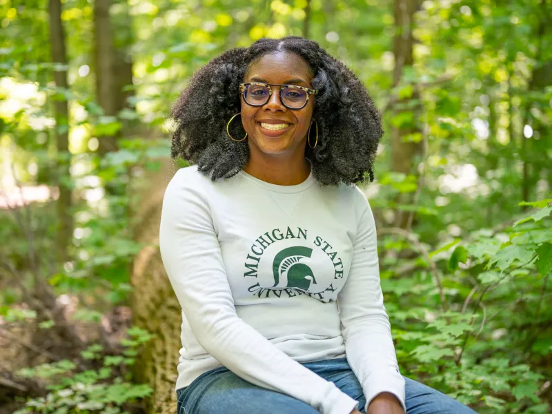 Asia L. Dowtin sits in the forest smiling