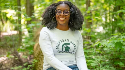 Asia L. Dowtin sits in the forest smiling