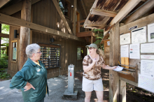 A campground host talks with a camper by a bulletin board.