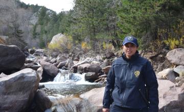 A female park ranger smiles as she stands in front of a river.